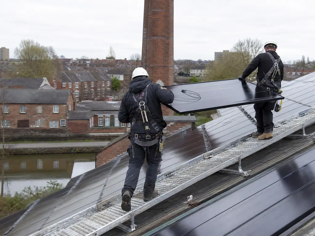 Installers carrying a panel across the sawtooth roof of a brick workshop in the East Midlands